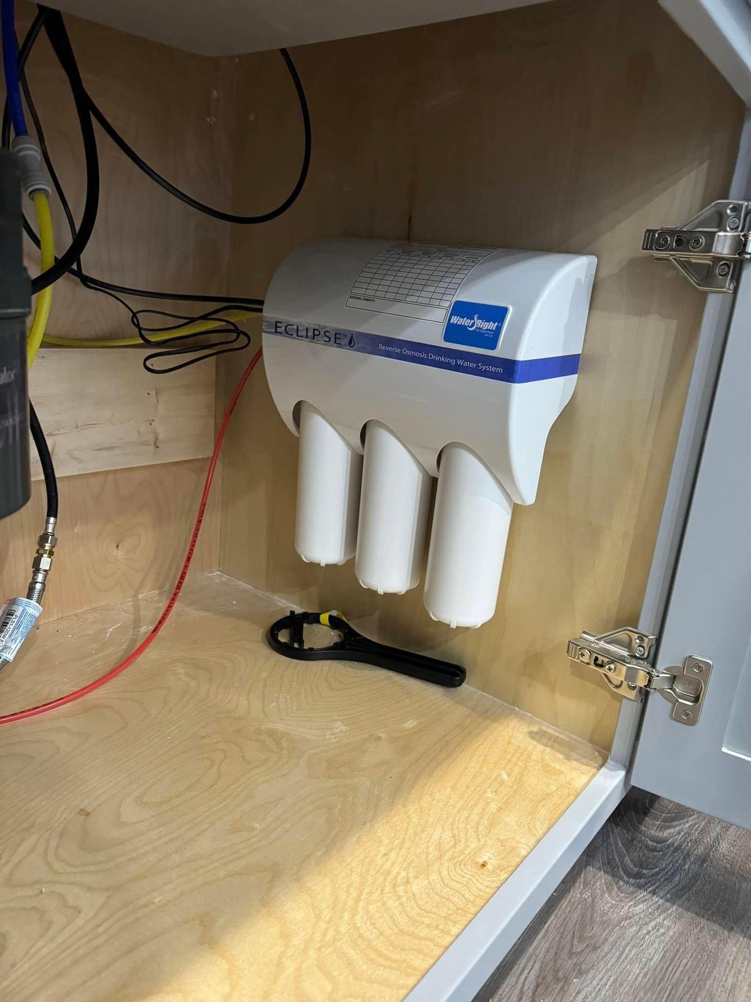 A water filter is sitting under a sink in a cabinet.