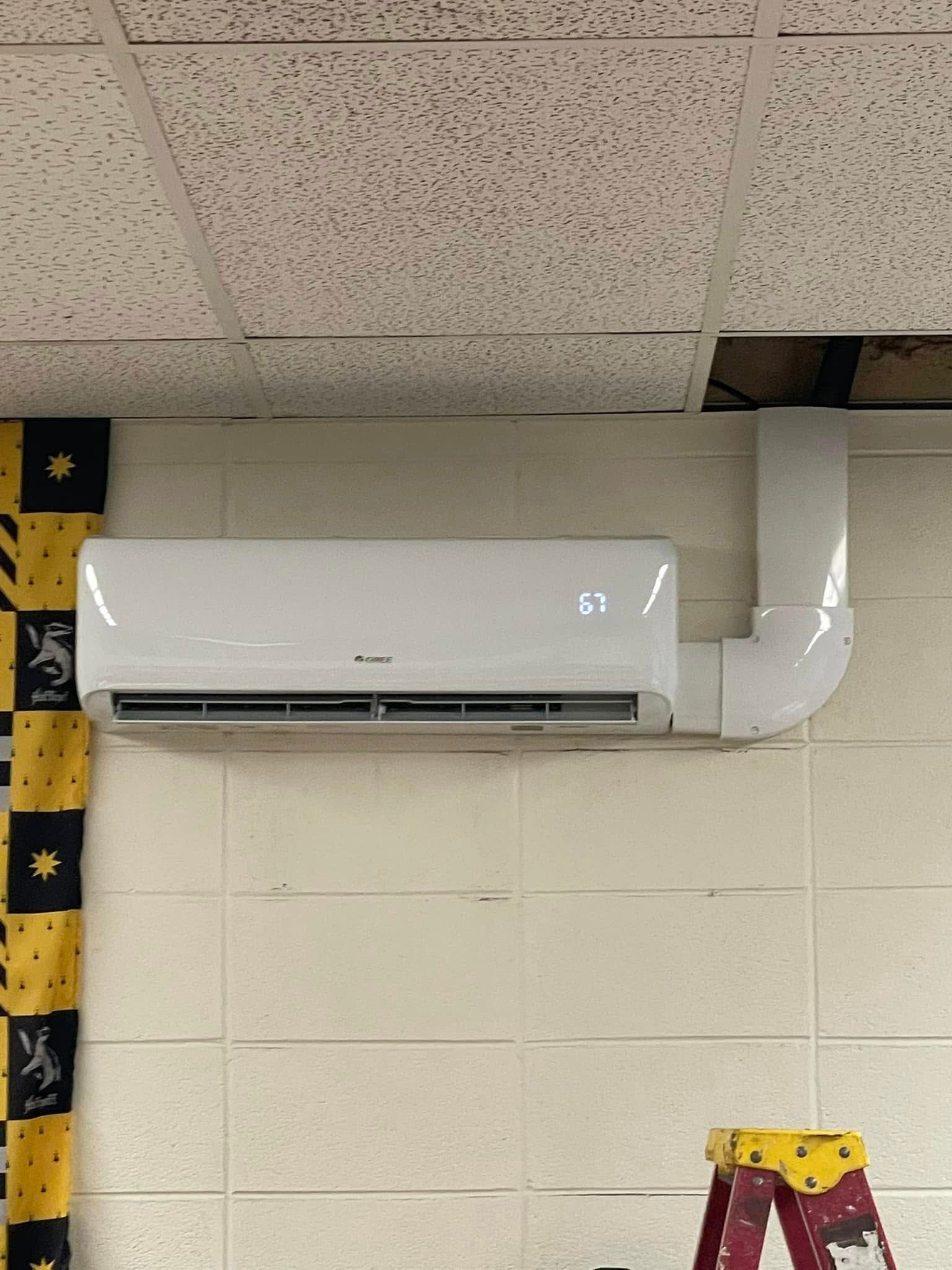 A white air conditioner is mounted on a wall next to a ladder.