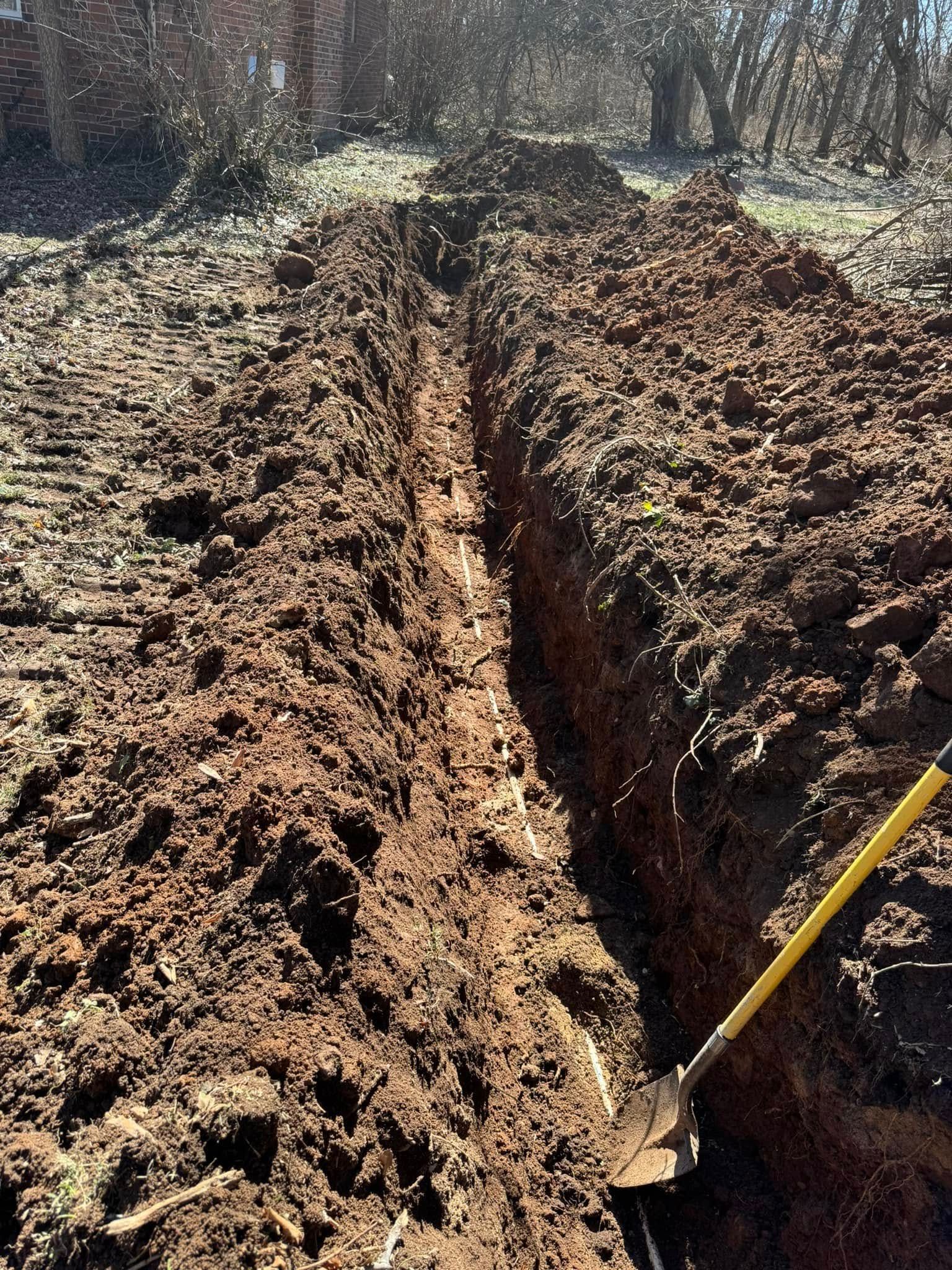A person is digging a trench in the dirt with a shovel.