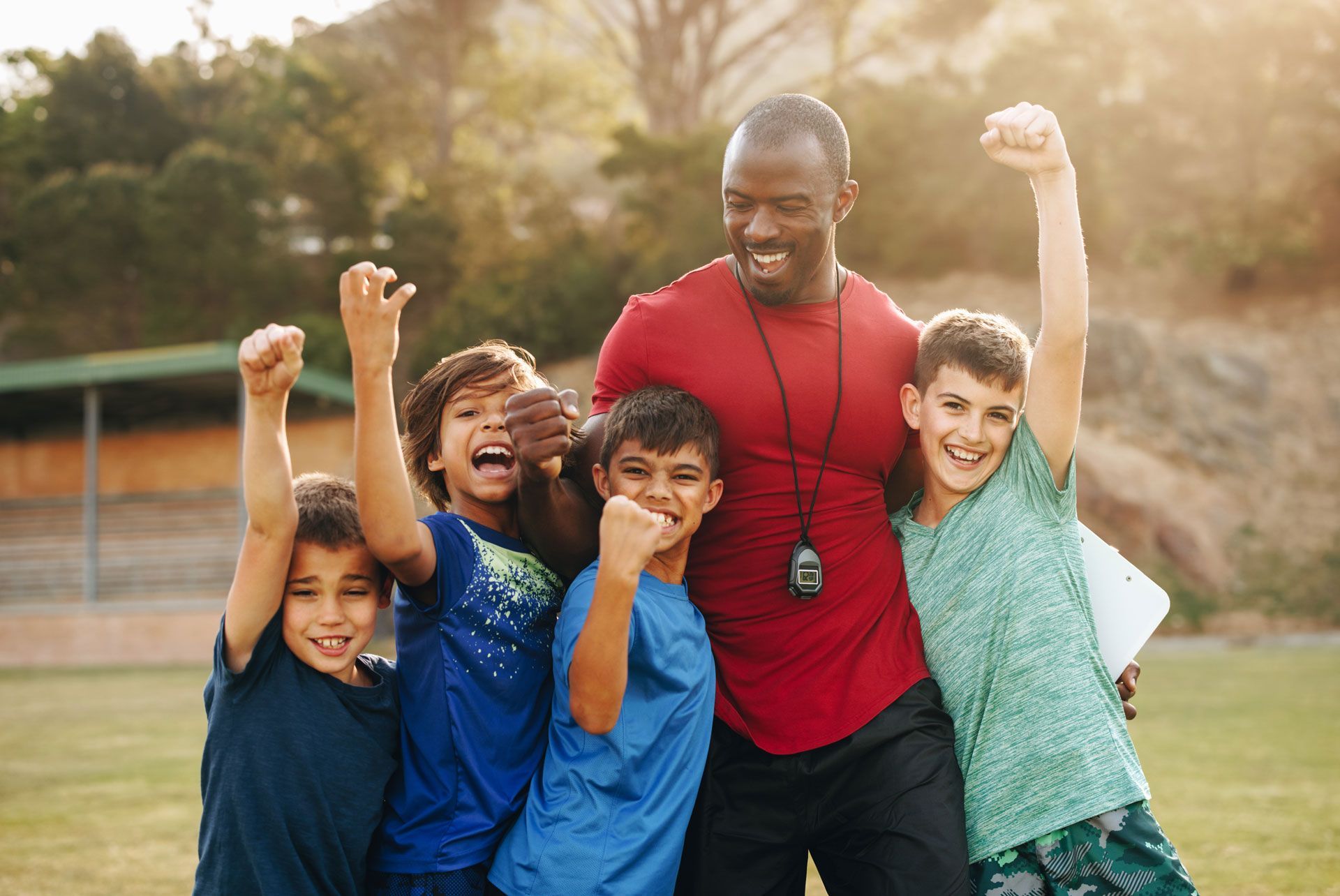 Coach with excited children on a field, arms raised in celebration.
