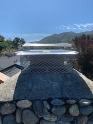 A chimney on top of a stone wall with mountains in the background.