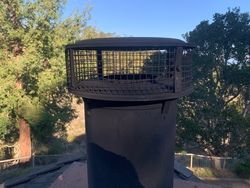 A black chimney on top of a roof with trees in the background.