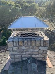 A stone chimney with a metal roof on top of it.