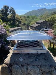 A metal chimney cap is sitting on top of a stone chimney.