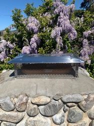 A stainless steel chimney cap is sitting on top of a stone wall.