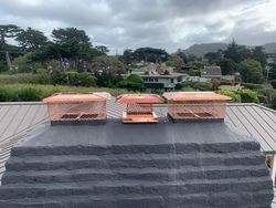 Three chimney caps are sitting on top of a brick chimney on a roof.