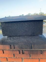 A brick chimney with a metal cover on top of it.