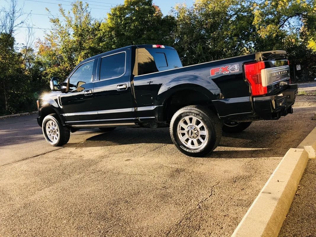 Black pickup truck parked in a lot, side view, with trees in the background.