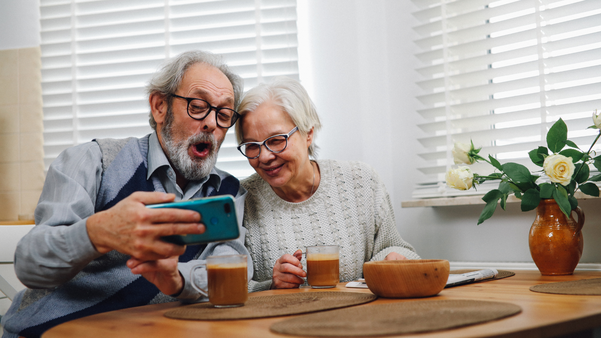 An elderly couple is sitting at a table looking at a cell phone.