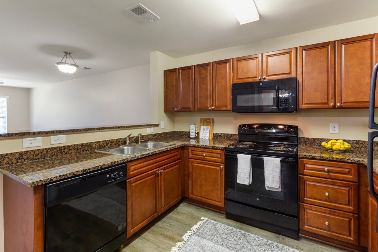 Kitchen with brown wood cabinets, granite countertops, double sink, and black appliances.