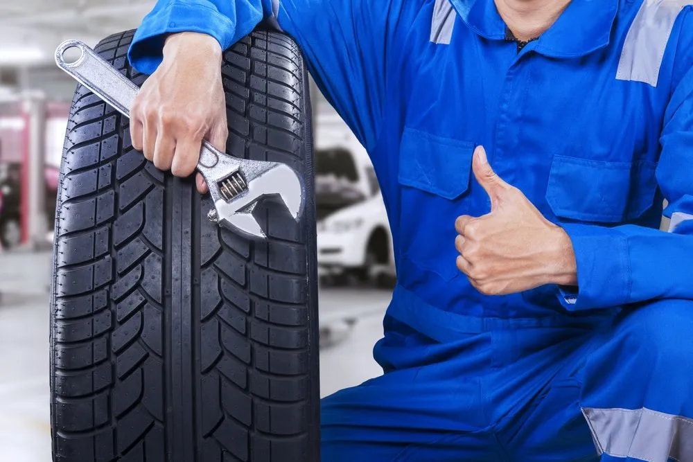 Mechanic in Blue Jumpsuit With Wrench, Thumbs Up Next to Tire in a Shop — Wheel Alignment Centre in Braitling, NT