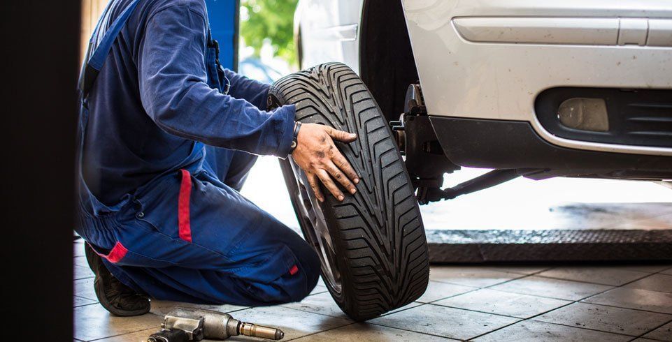 Mechanic in Blue Coveralls Replacing a Car Tire in a Garage — Wheel Alignment Centre in Braitling, NT