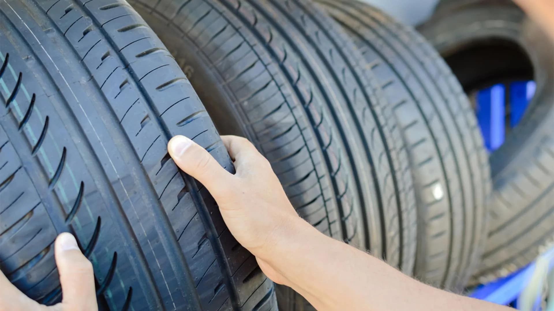 Person's Hands Examining a New Car Tire. Multiple Tires Are Stacked — Wheel Alignment Centre in Braitling, NT