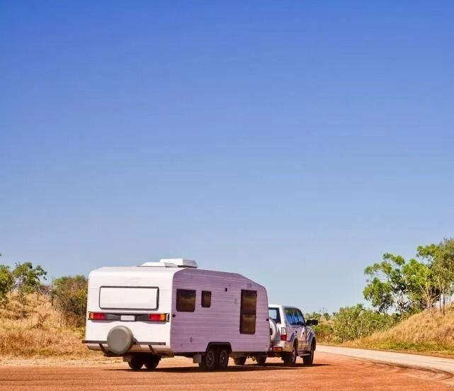 White RV trailer being towed on a dirt road under a clear blue sky. — Wheel Alignment Centre in Braitling, NT