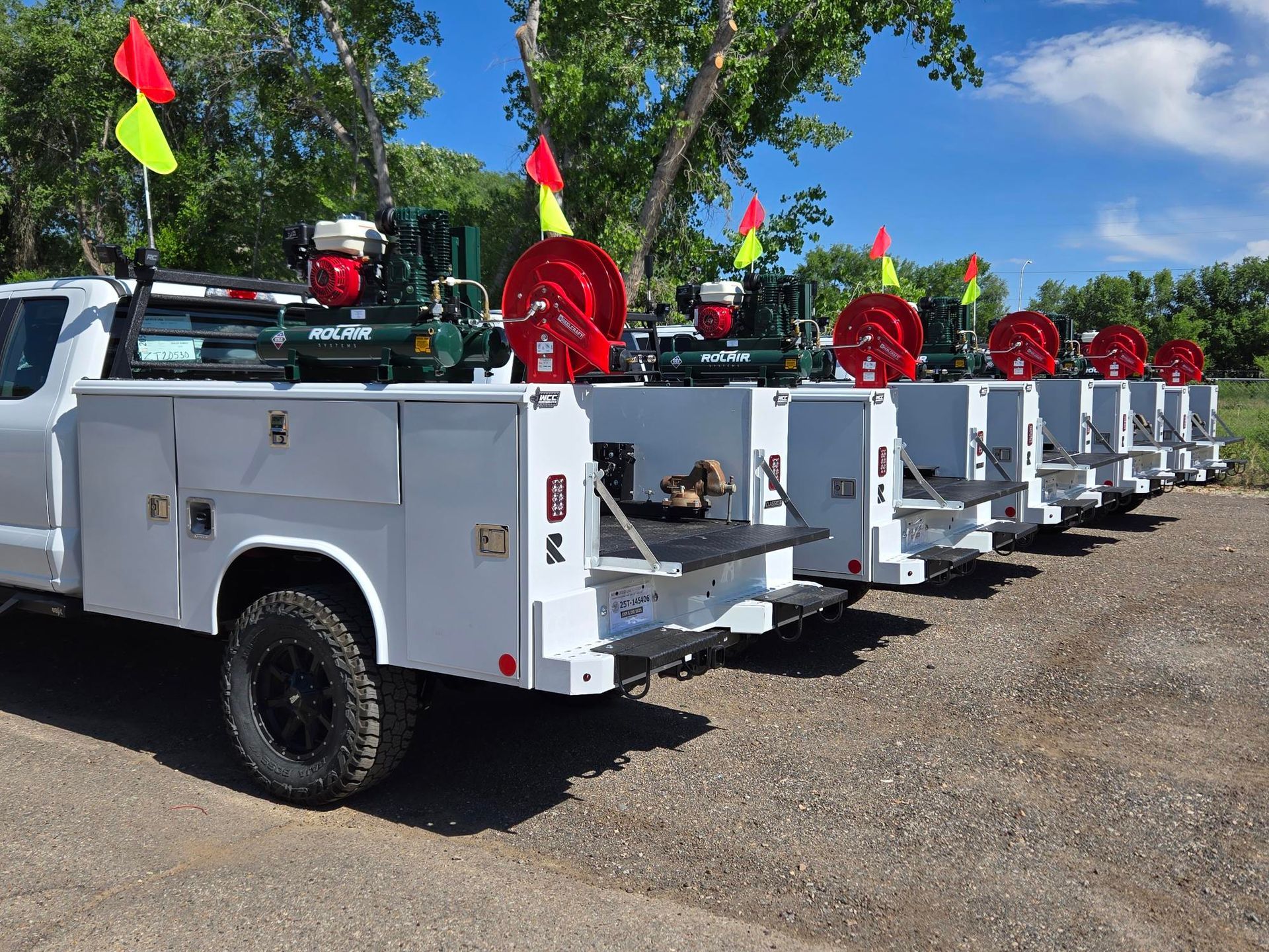 A row of white utility trucks are parked in a gravel lot.