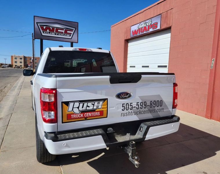 A white truck is parked in front of a wrap shop