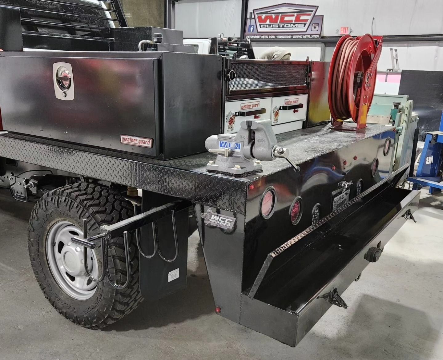 A black truck with a toolbox on the back is parked in a garage.