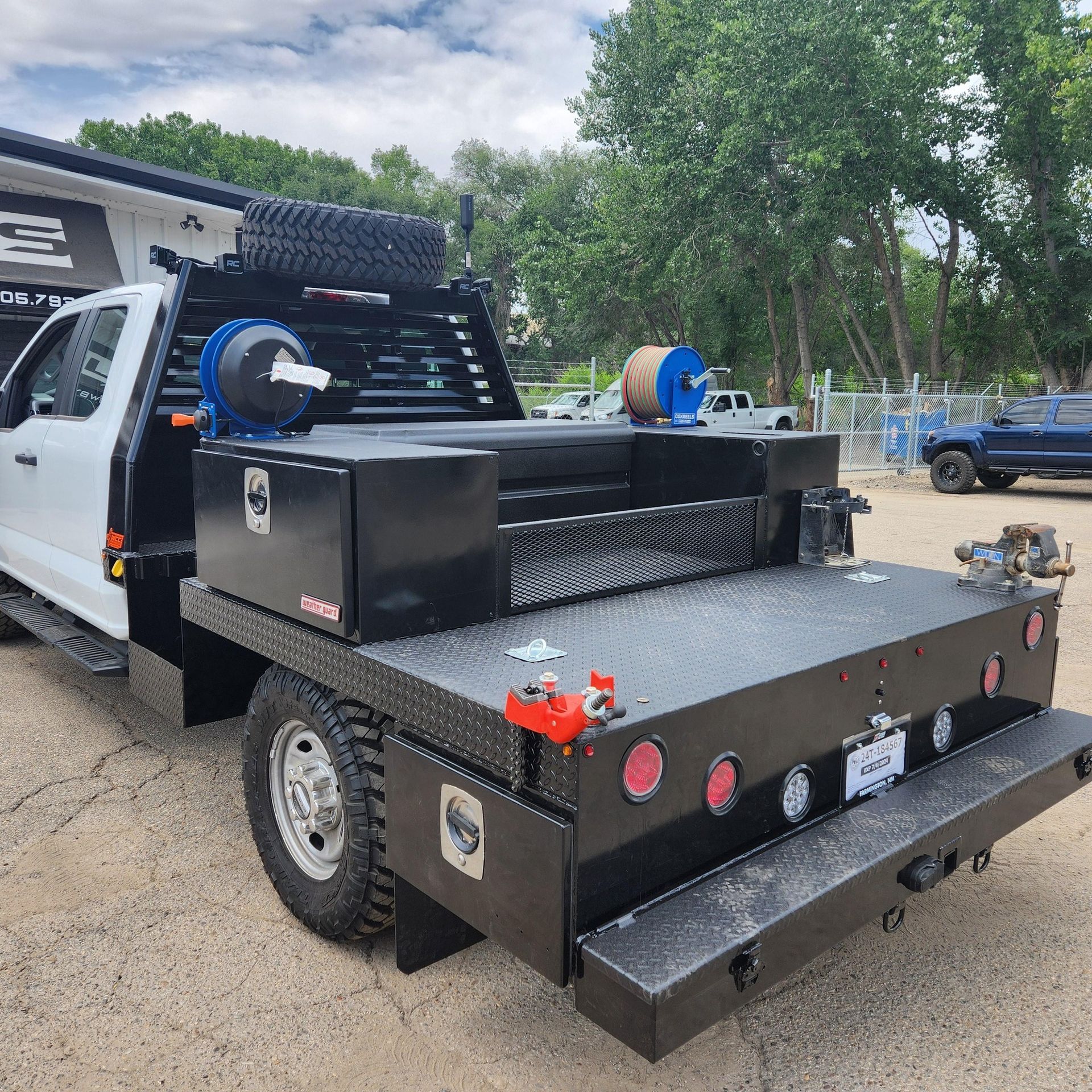 A white truck with a black bed is parked in a dirt lot.