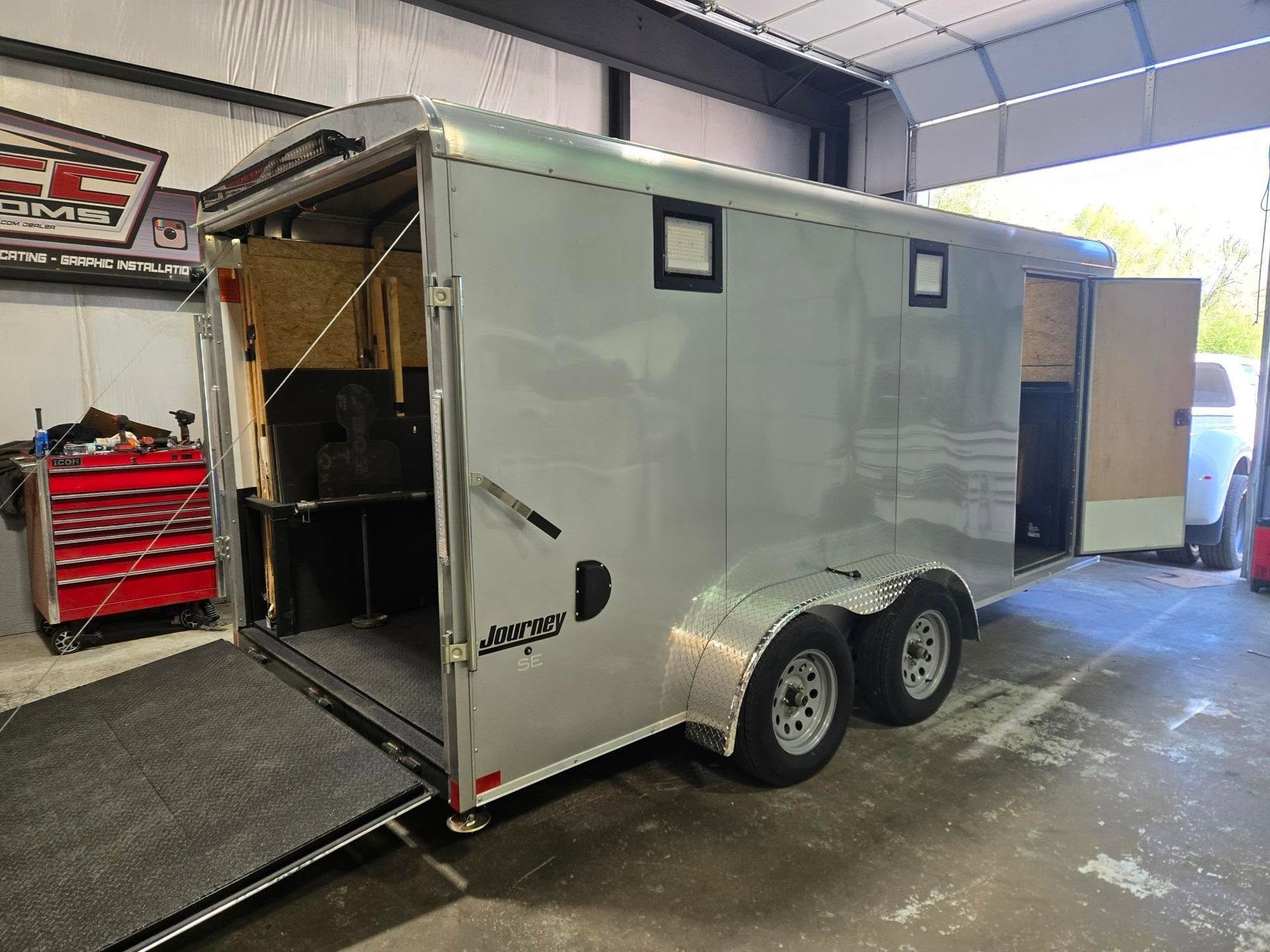 A silver trailer is parked in a garage with the door open.
