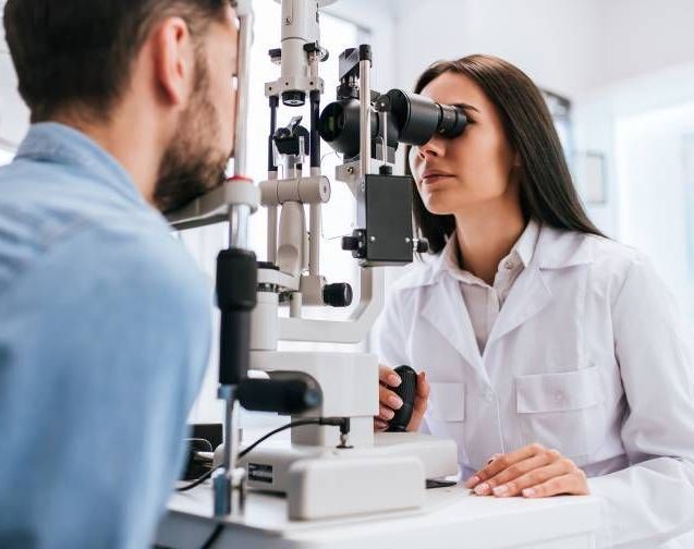 The female optometrist checking the eye of the guy in the blue shirt — Optometrist in Wallsend, NSW