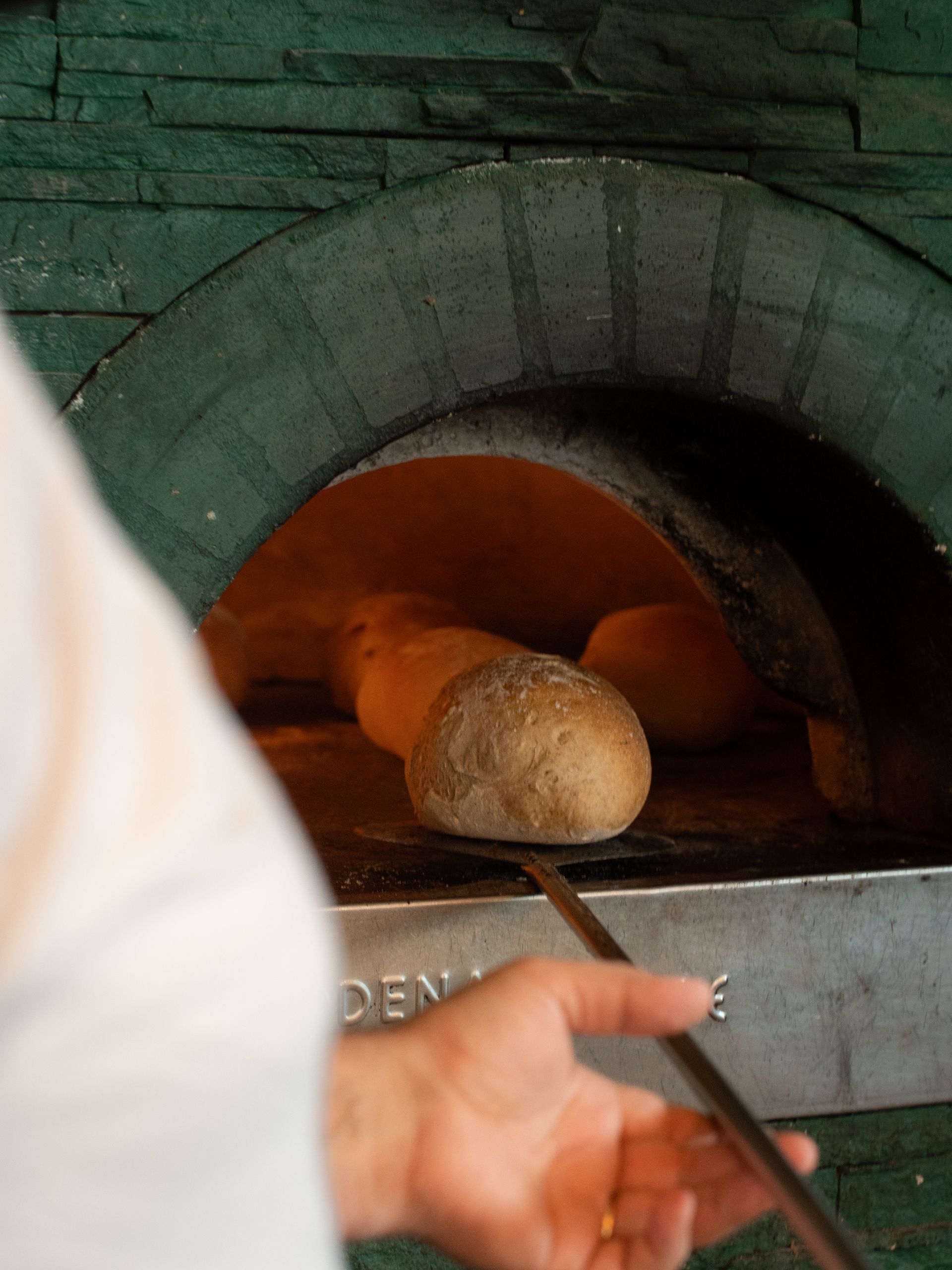 Il fornaio mette il pane nel forno caldo con una pala. L'interno del forno in pietra si illumina di arancione.