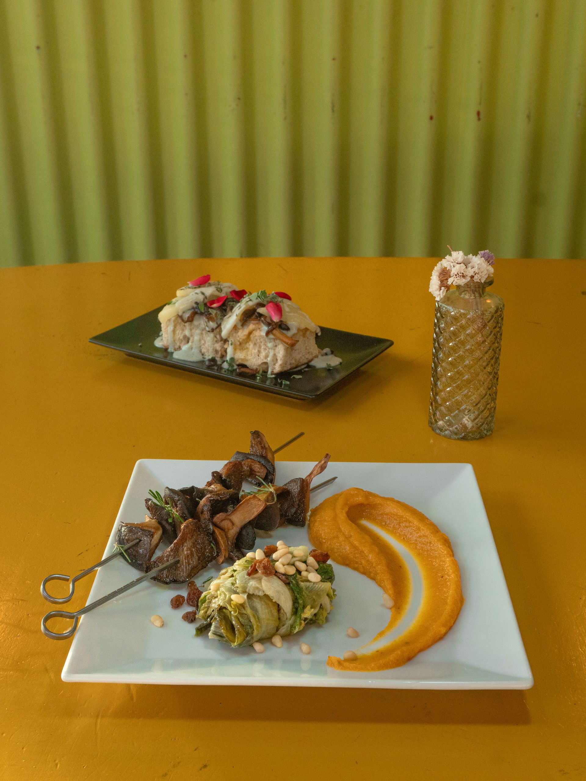 Piatto di spiedini, salsa e involtino; un altro piatto con riso. Sfondo giallo.