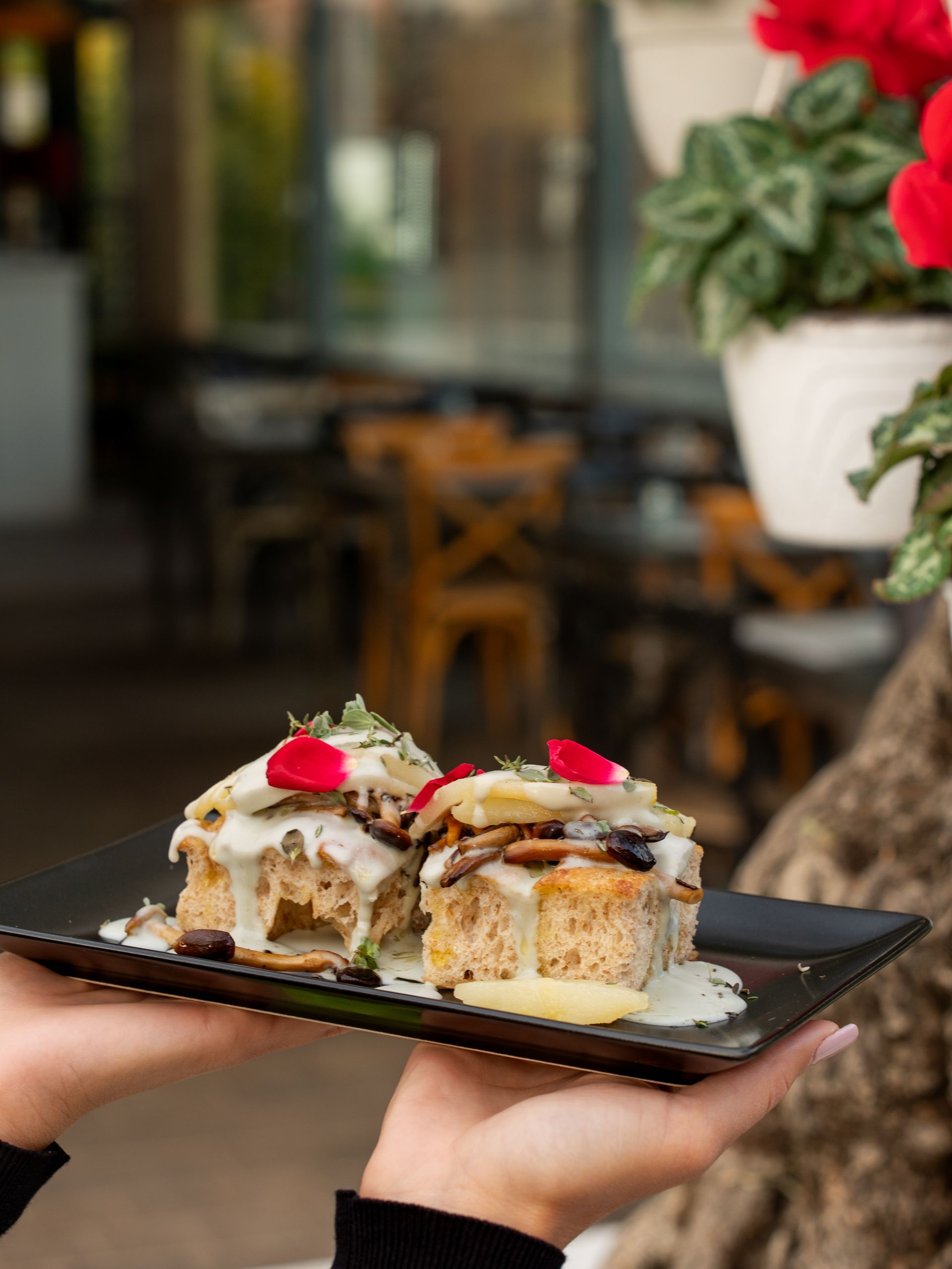 Due pasticcini ai funghi con salsa cremosa su un piatto nero, tenuti da una persona all'aperto.