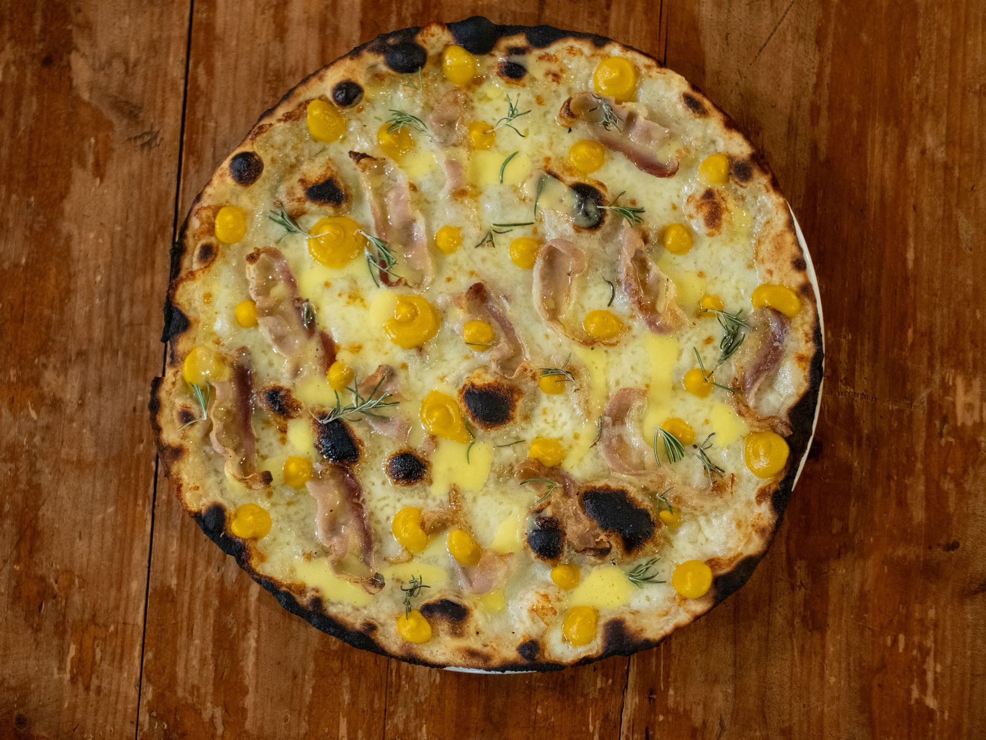 Pizza con mais, pancetta ed erbe aromatiche su un tavolo di legno.