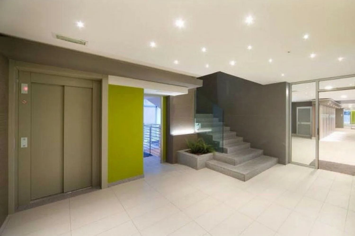 Moderna hall di un edificio con ascensore, scale e parete decorativa verde.