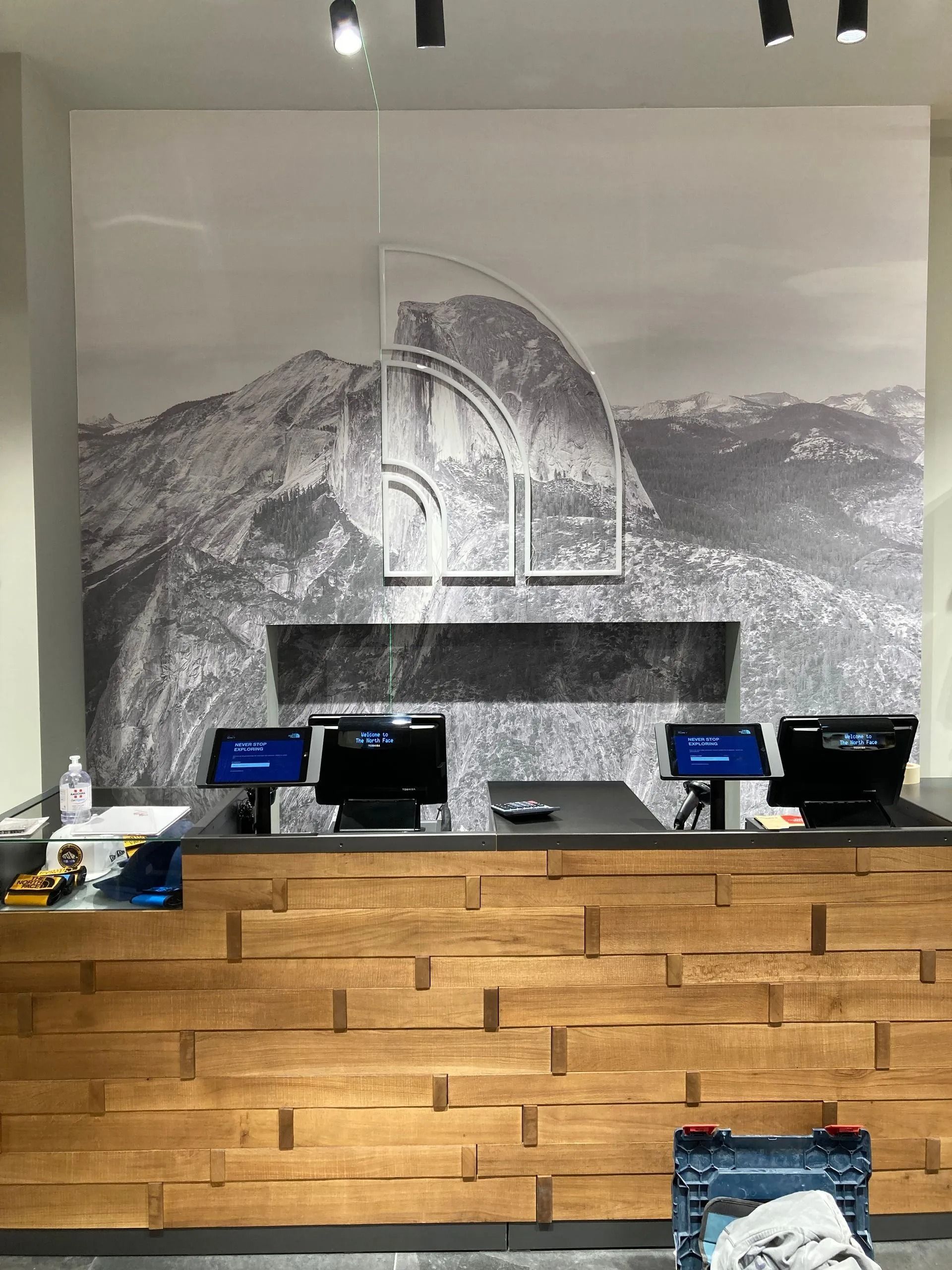 Bancone della cassa con due monitor nel negozio The North Face, pannelli in legno, sfondo con immagine di montagna.