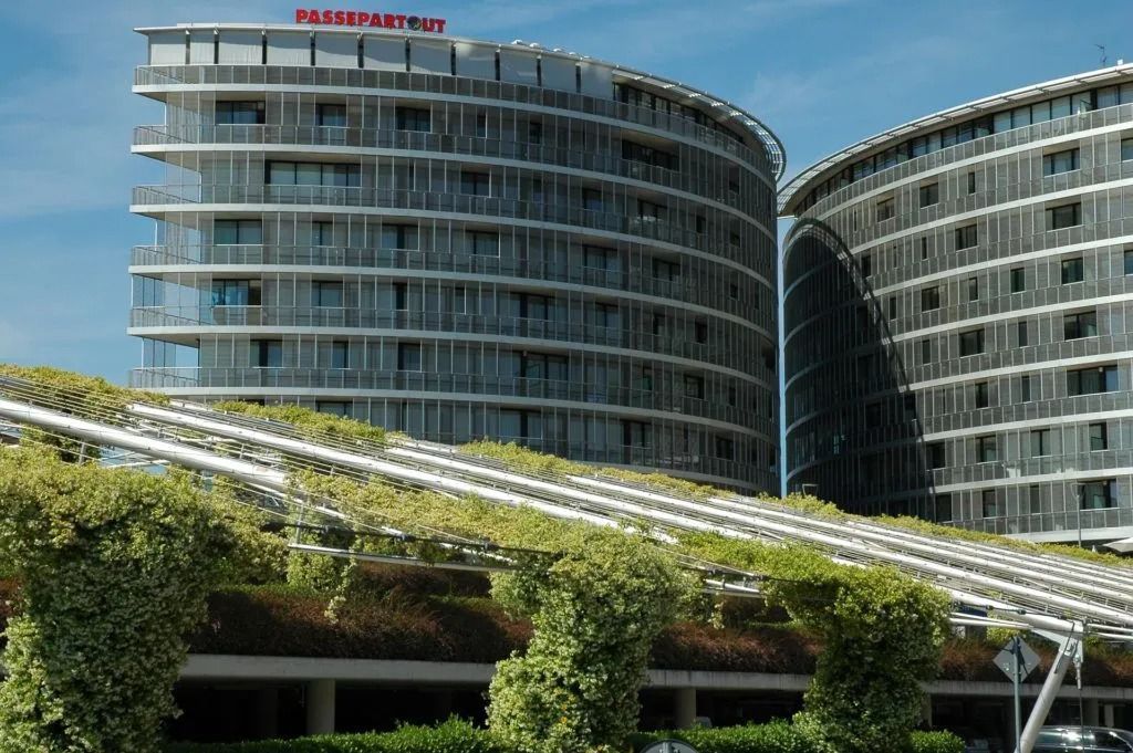 Edificio moderno e curvo con linee verticali e tetto verde, con la scritta 