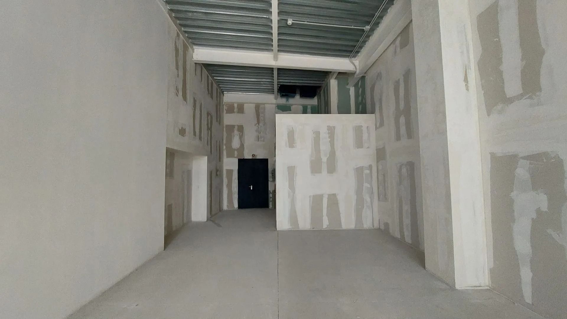 Interno di un edificio in costruzione; le pareti sono grezze con cartongesso a vista; in lontananza si vede un portone scuro.