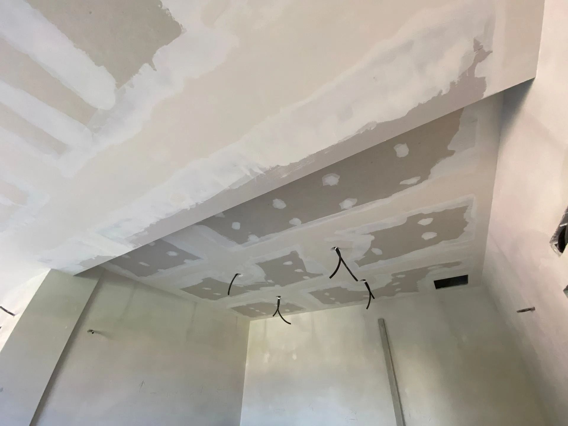 Controsoffitto in cartongesso in costruzione, con giunzioni nastrate visibili e fori per viti riempiti; fili neri pendono.