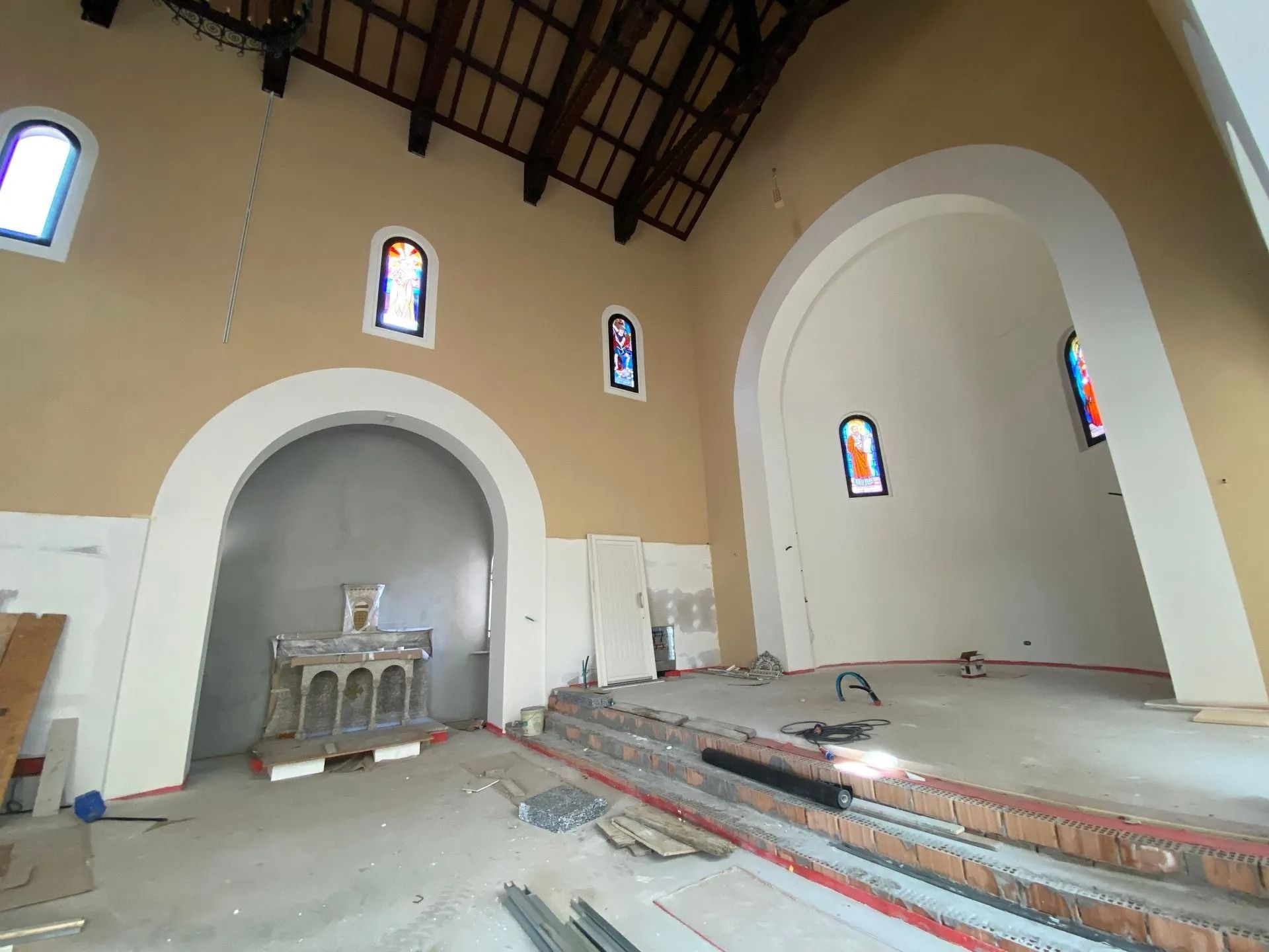 Interno di una chiesa in costruzione; nicchie ad arco, vetrate colorate e travi a vista sul soffitto.
