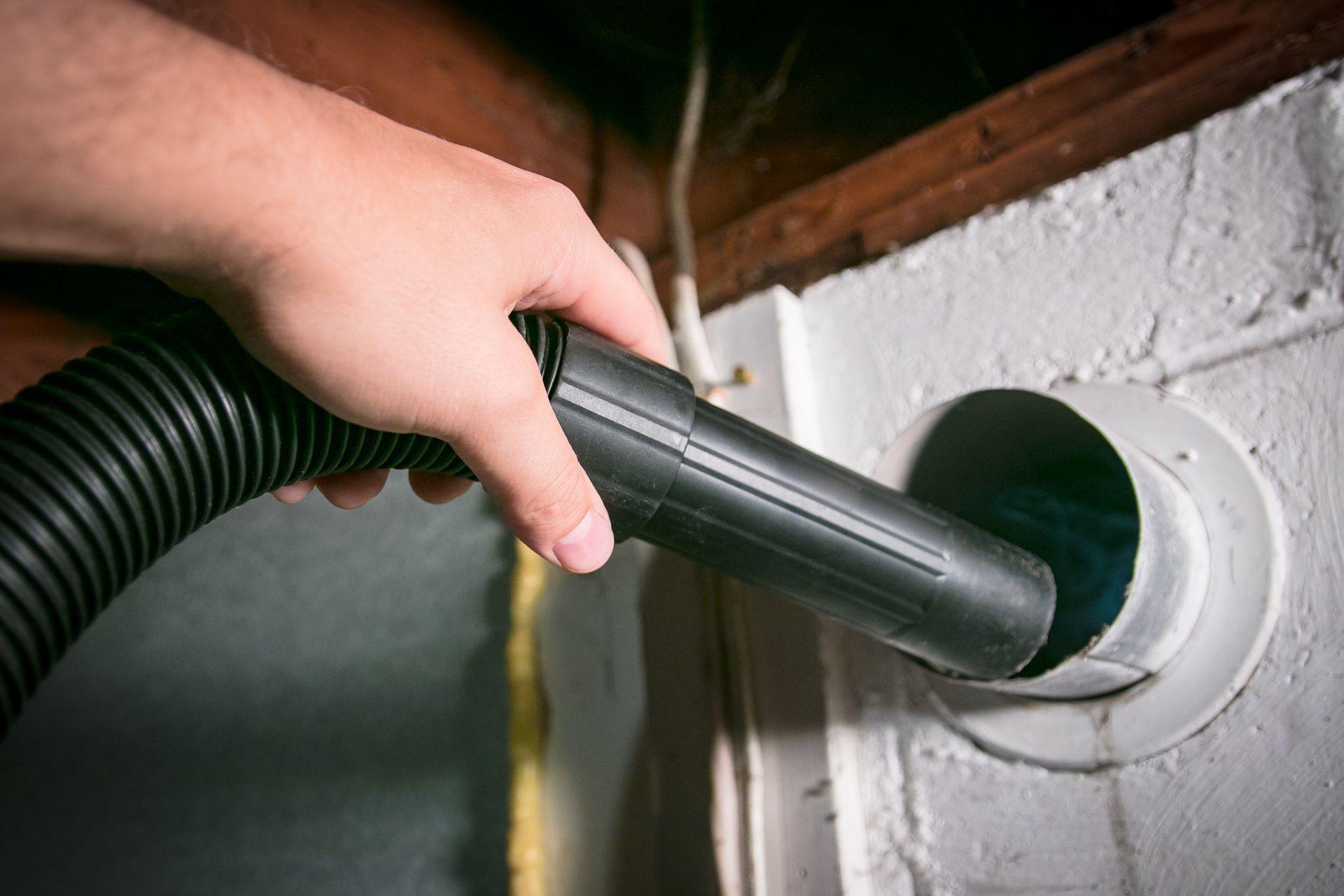 Person vacuuming a vent with a black hose in a basement.