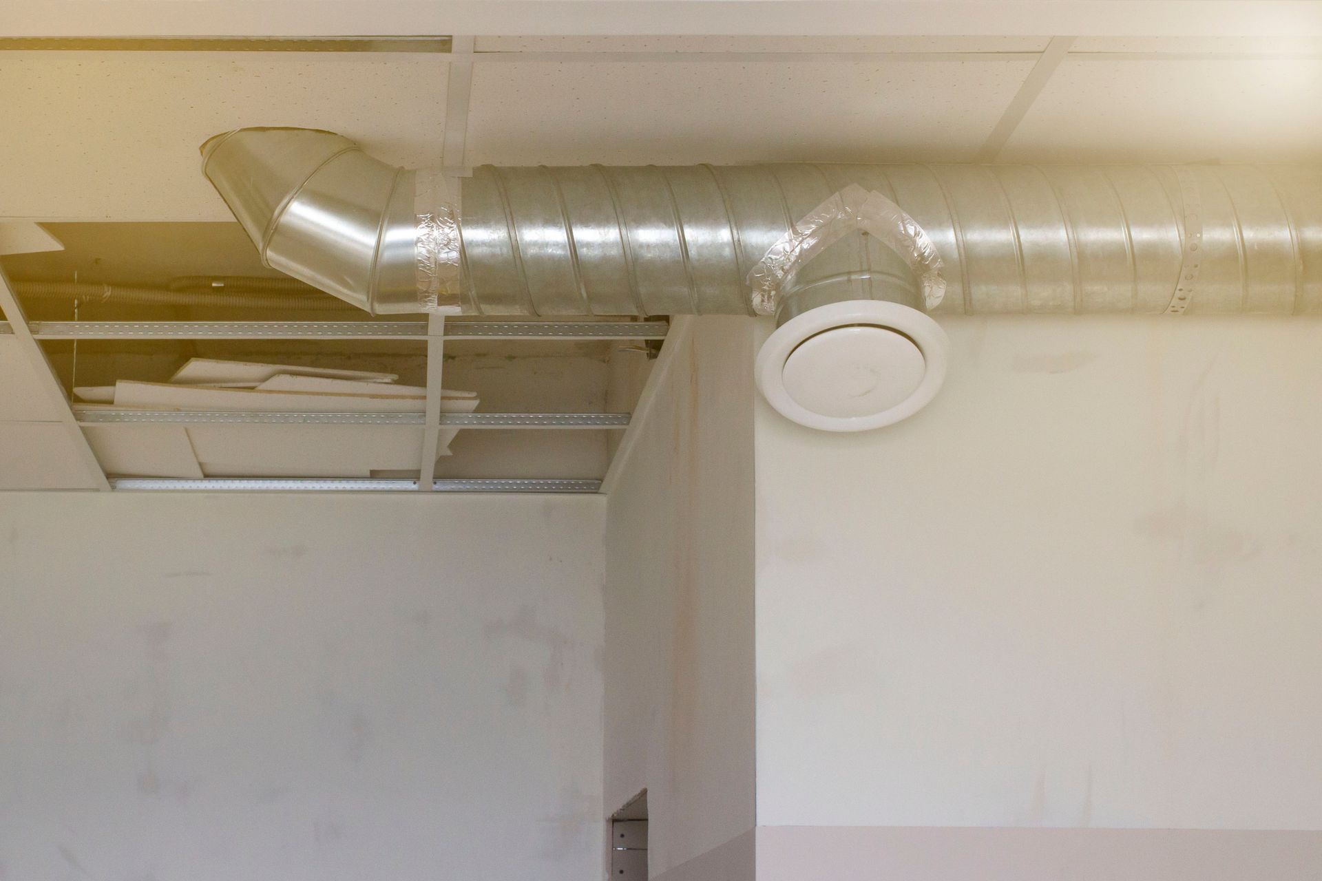 HVAC ductwork and vent in a room with missing ceiling tiles, showing construction or damage.