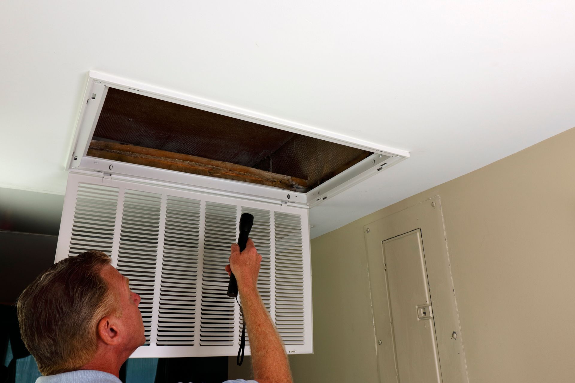 Man inspecting an air vent in a ceiling with a flashlight.