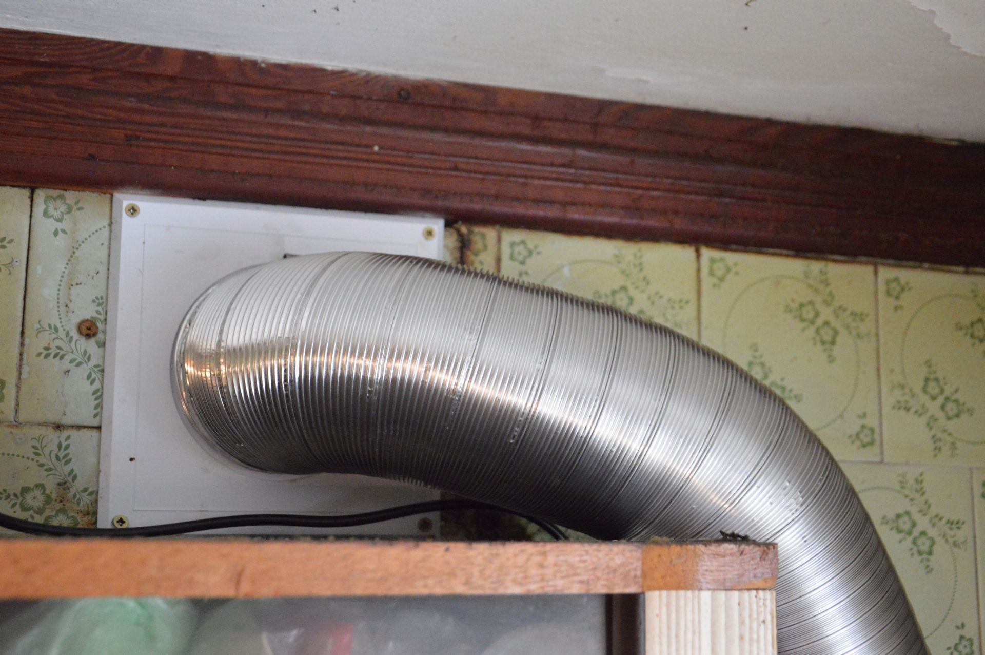A flexible metal vent pipe connected to a white square on a wall, above a shelf.