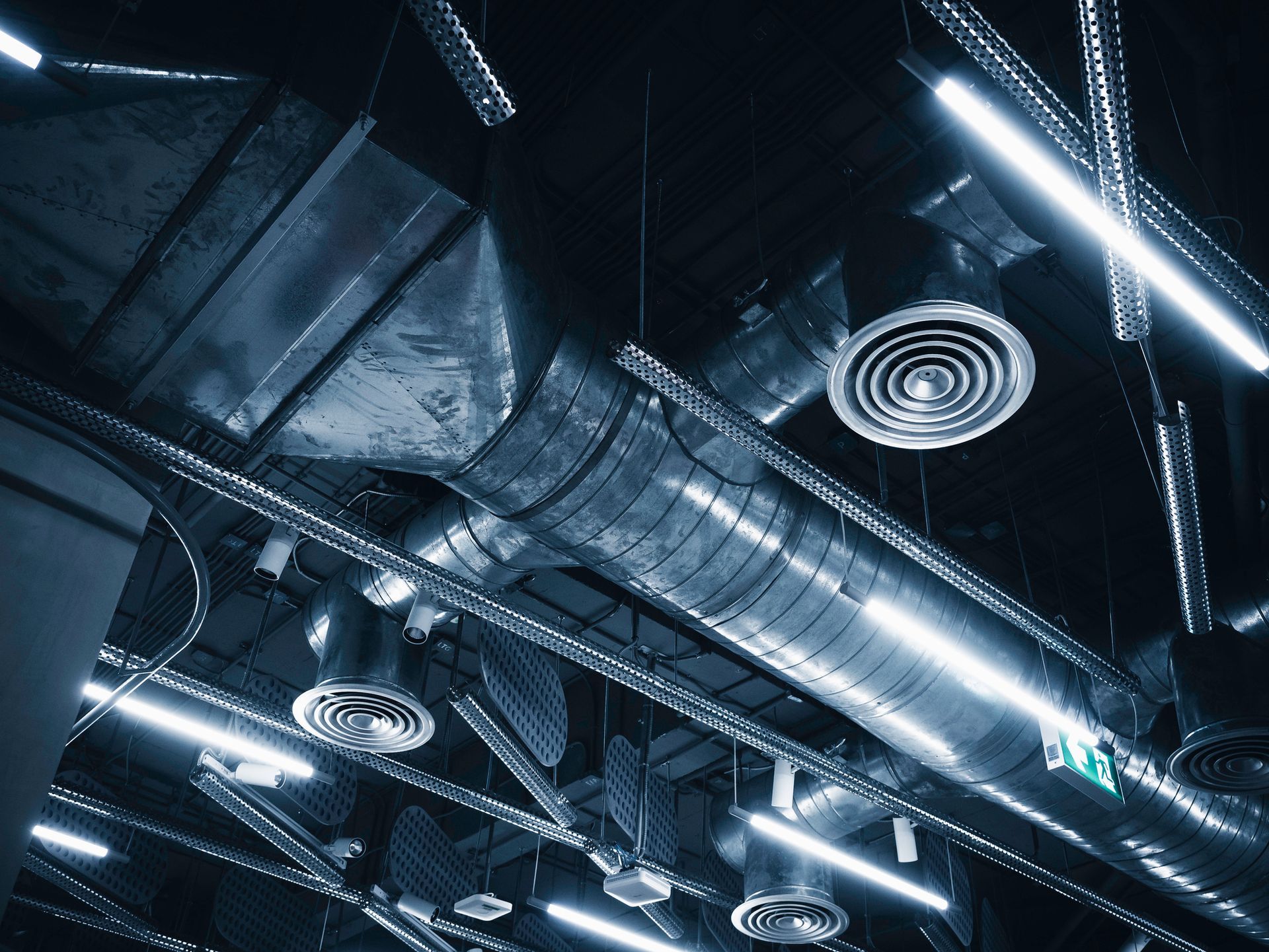 Air ducts and lighting in a modern industrial-style ceiling, shot from a low angle. Air ducts and lighting in a modern industrial-style ceiling, shot from a low angle.