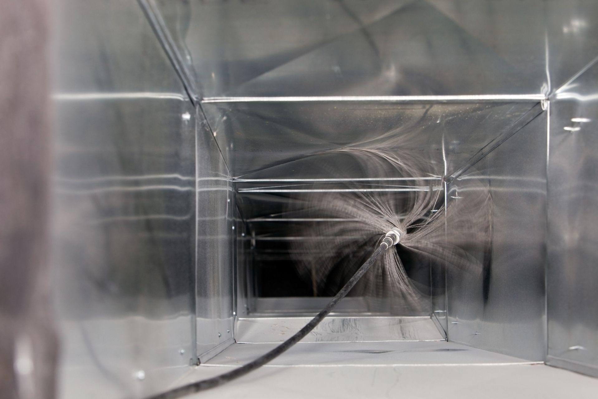 Inside a rectangular metal duct, a cable with debris radiates from the center.