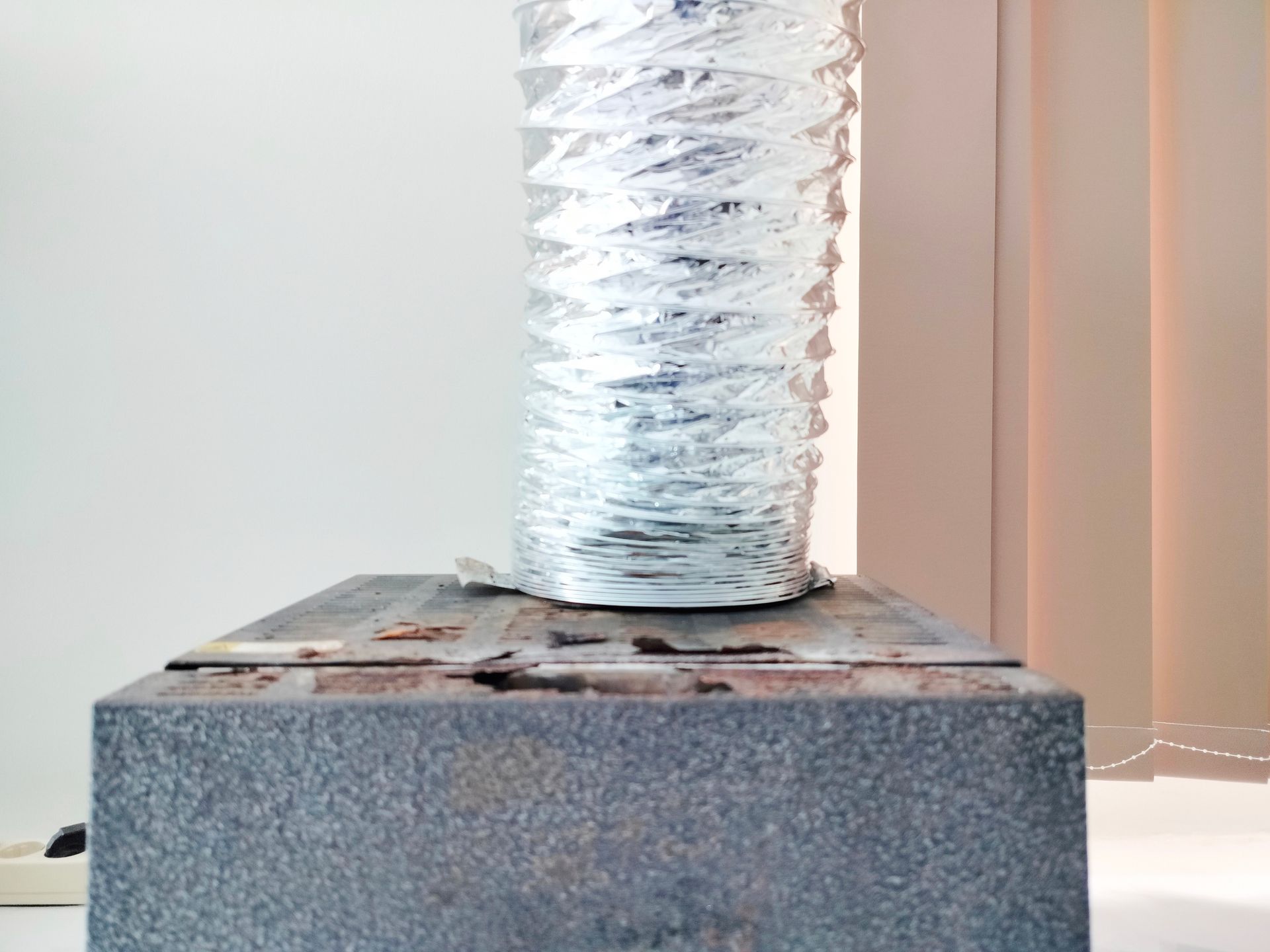 Silver vent pipe connected to a gray box, against a white wall.