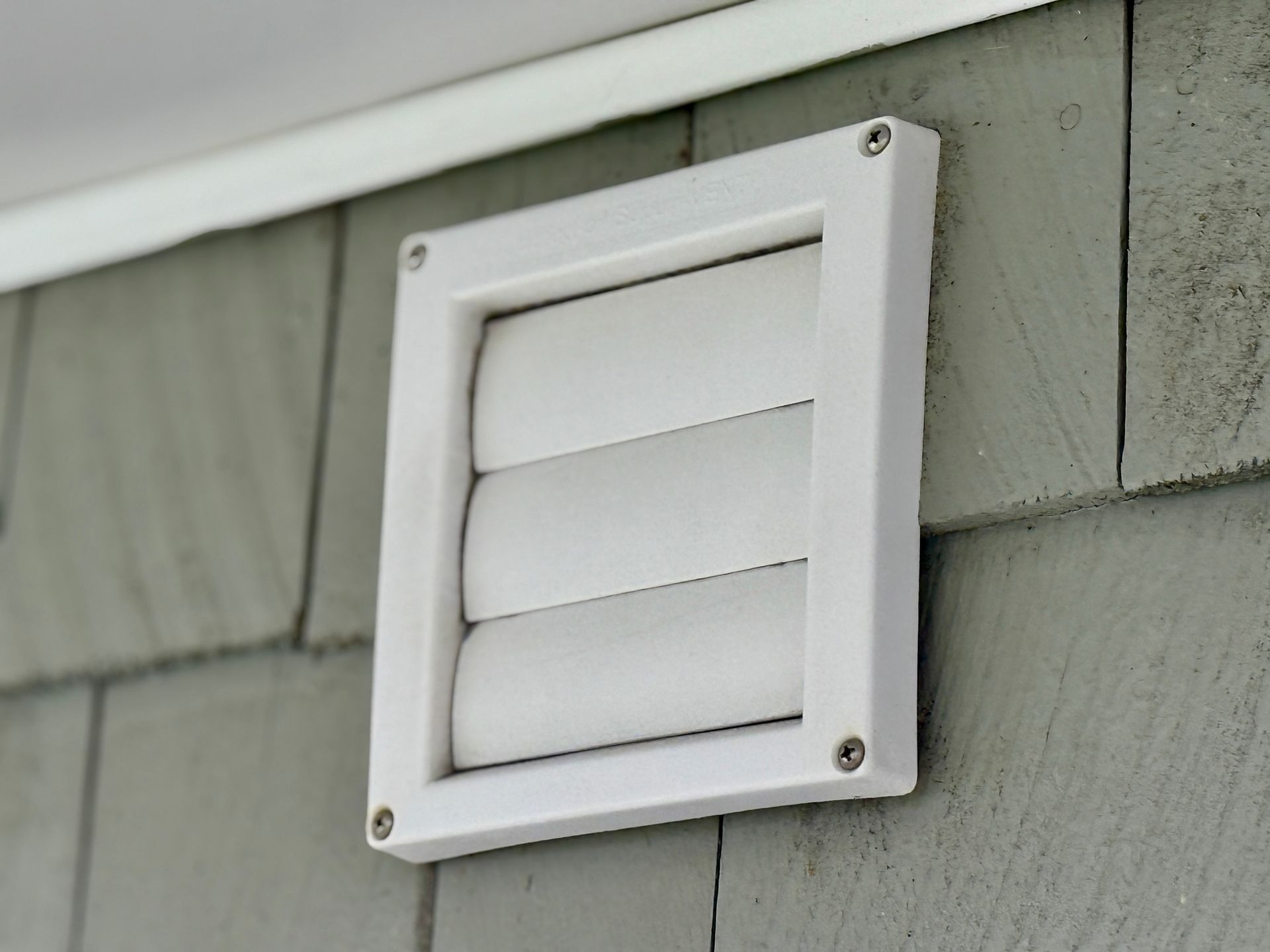 White vent cover on gray siding, releasing air from a building. White vent cover on gray siding, releasing air from a building.