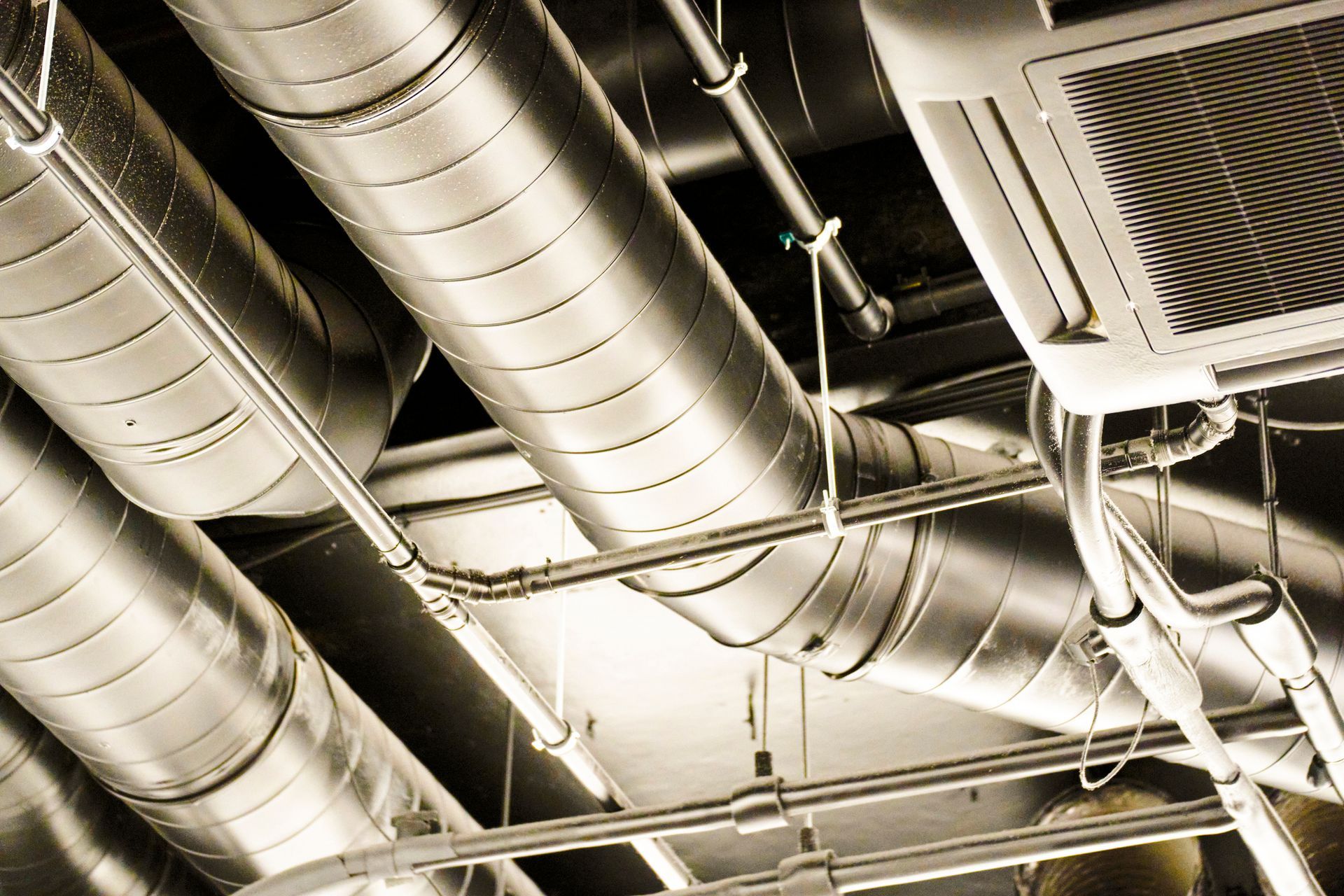 Silver HVAC ducts and pipes on a ceiling, industrial setting.