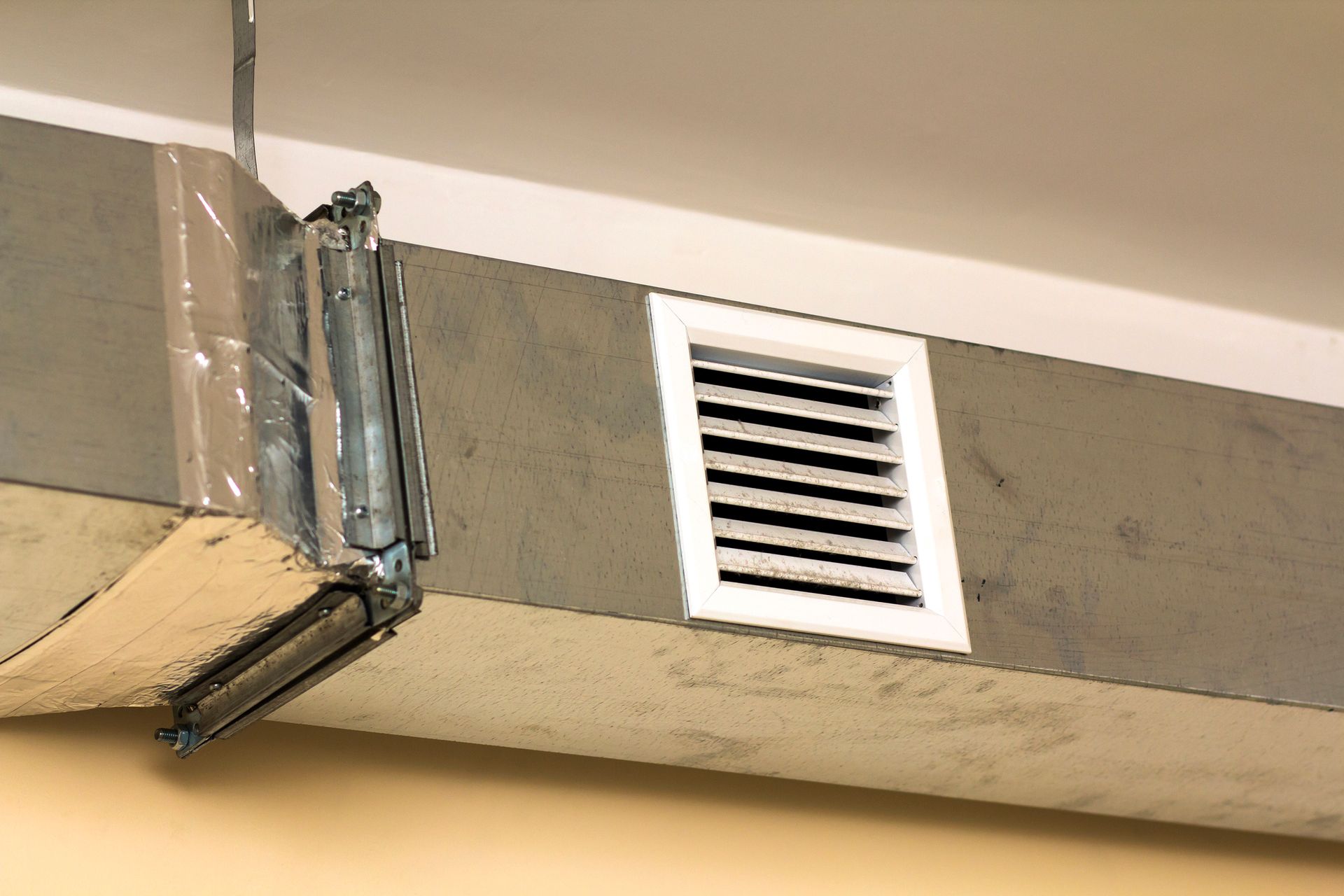 Air vent in a ceiling, connected to ductwork with metallic tape and clamps.