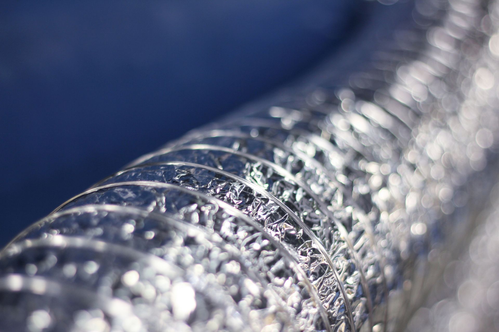 Flexible silver ducting, curled against a blurred blue background.
