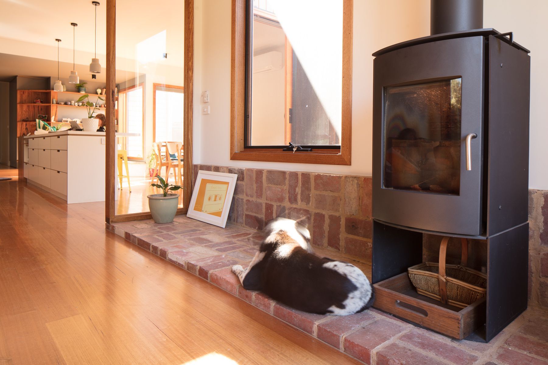 A dog is laying on a brick fireplace next to a wood stove.