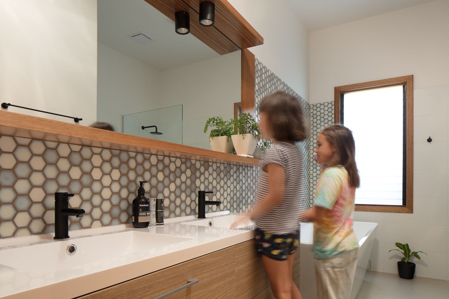 Two young girls are brushing their teeth in a bathroom.