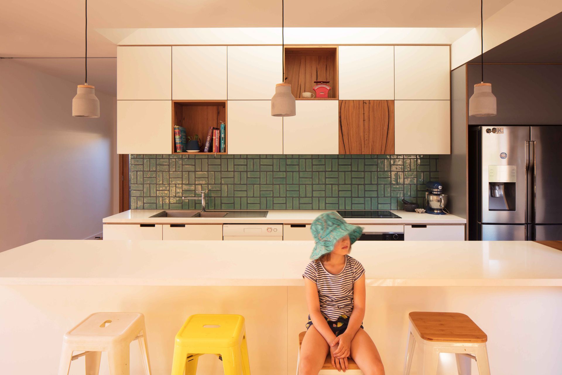 A little girl is sitting on a stool in a kitchen.