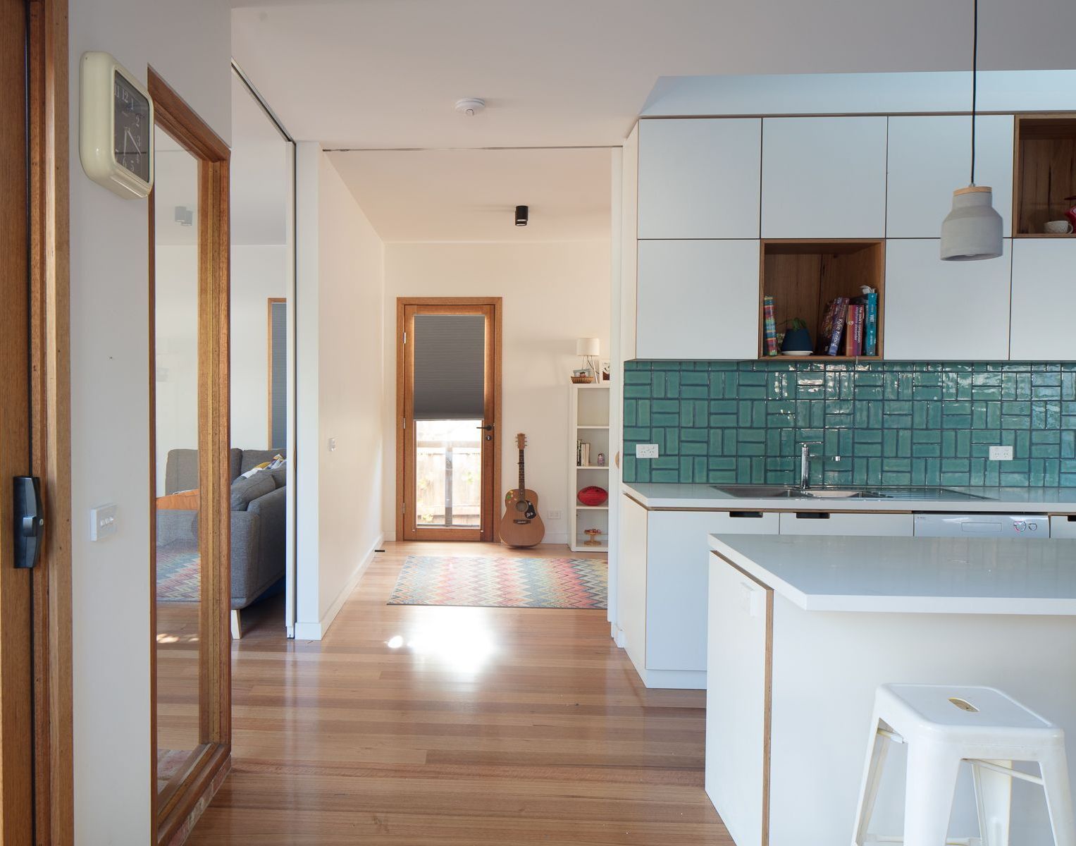 A kitchen with white cabinets and green tiles and a guitar on the counter.