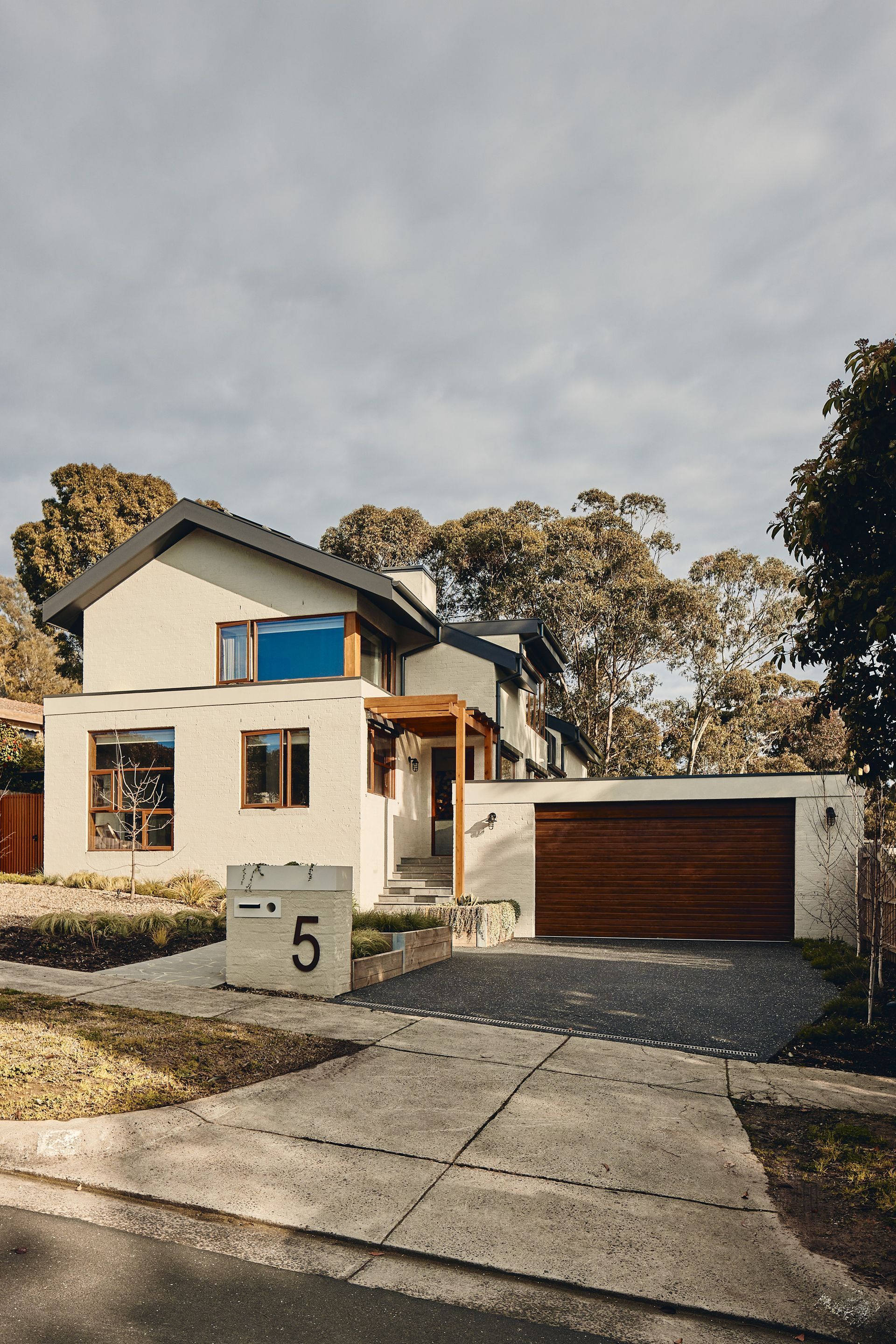 A white house with a brown garage door is sitting on a residential street.